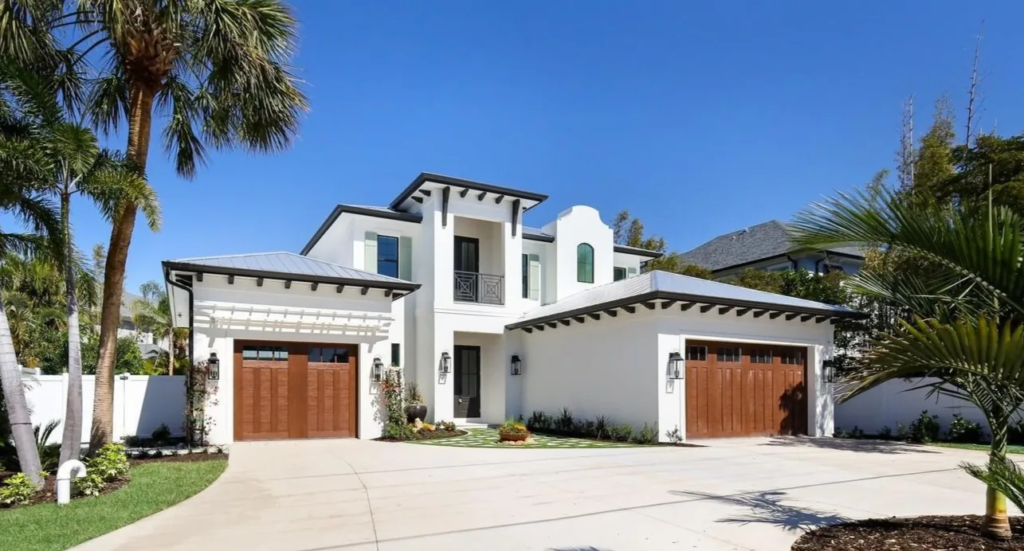 White coastal custom home with wood garage doors and palm trees